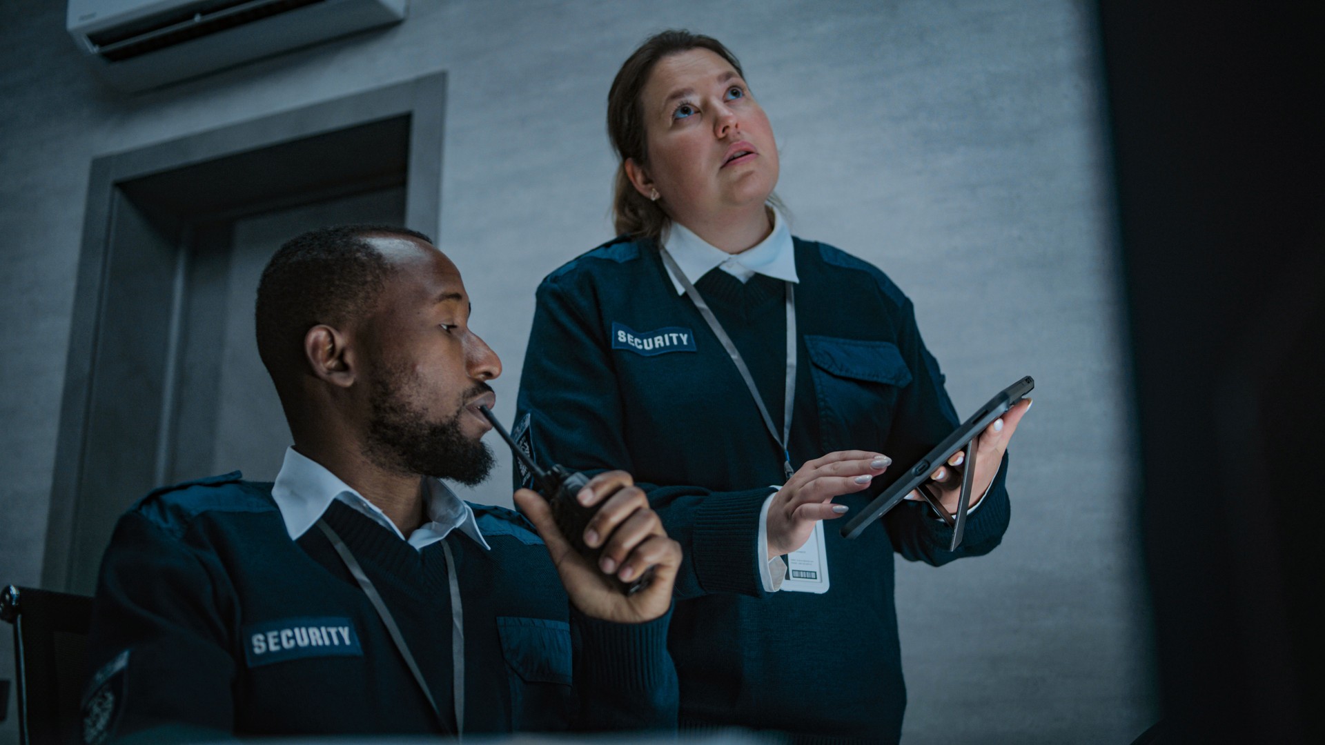 Female security officer stands and uses tablet. African American dispatcher talks in walkie talkie