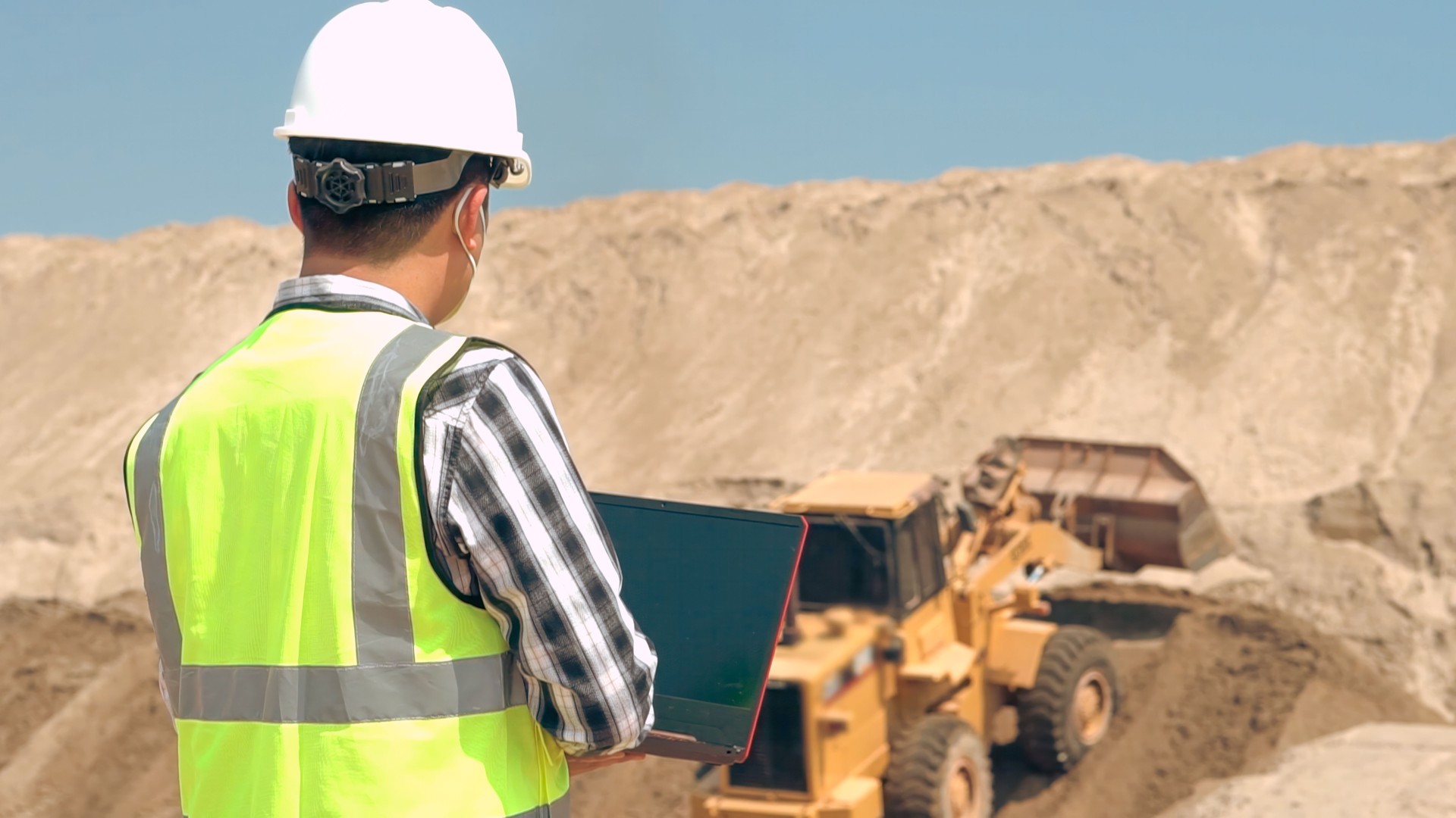 Asian Engineer uses laptop to check sand and stone inventory at construction site.